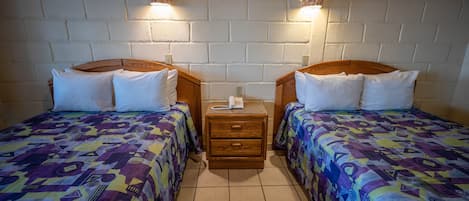 A room with two beds, each with a wooden headboard, a small bedside table with a phone, and patterned bedding.
