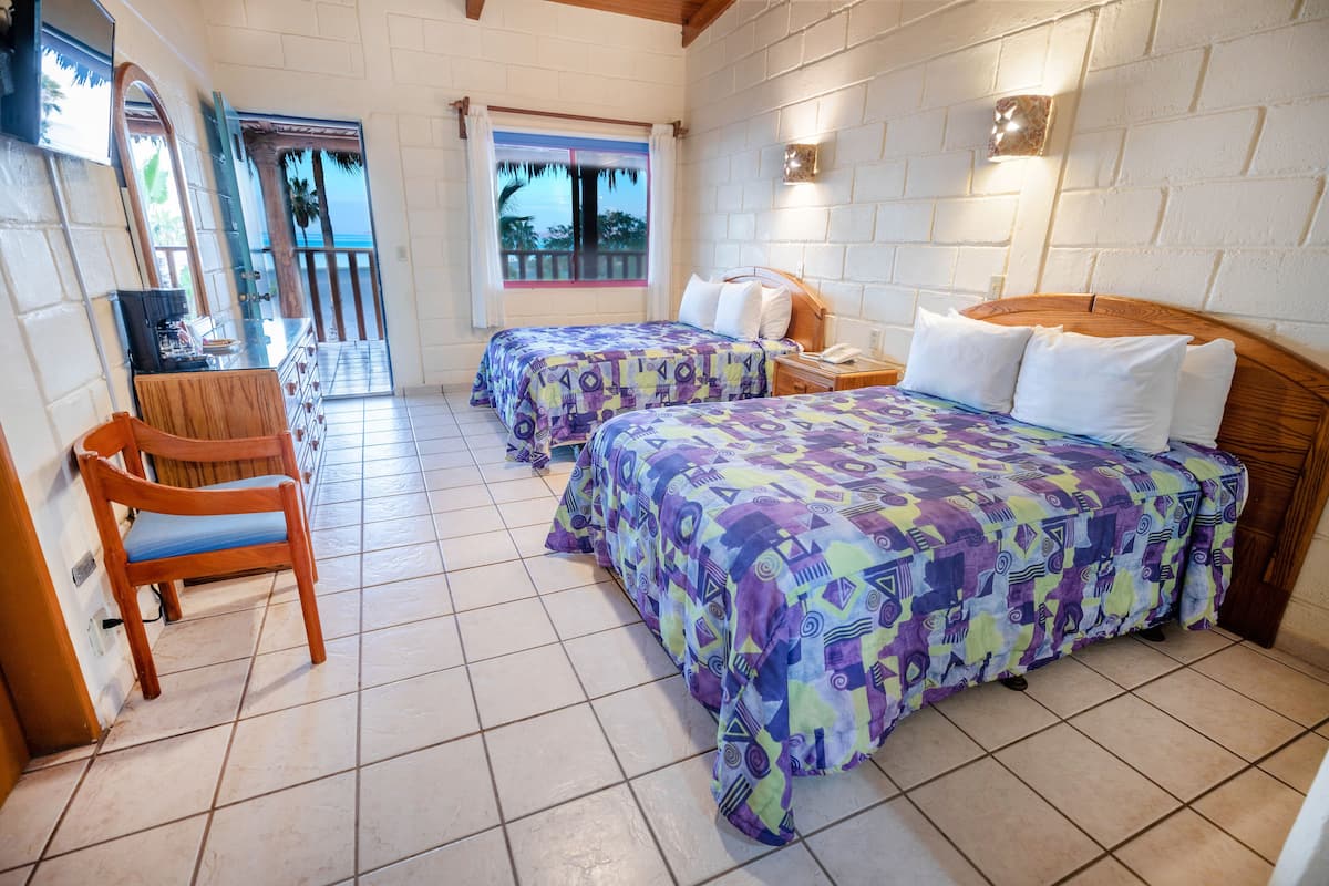 A hotel room with two beds, a wooden chair, a desk, and a window with a view of the ocean.