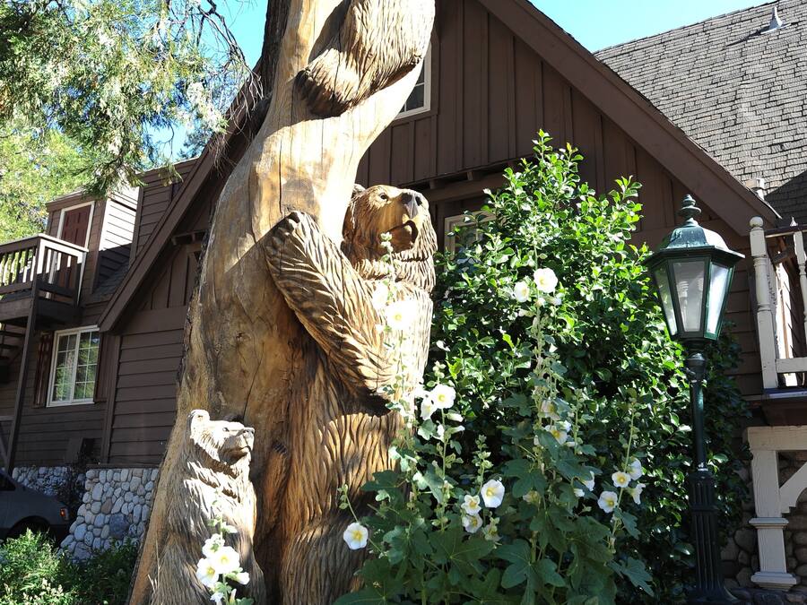 Une grande sculpture d’arbre représentant un ours sculpté, un mur de pierre et un bâtiment avec un balcon en arrière-plan.