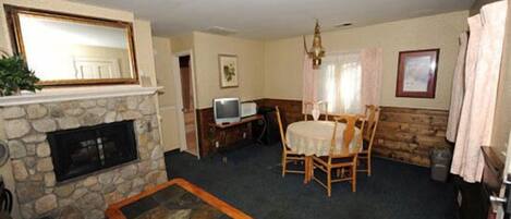 A living room with a stone fireplace, a television, a dining table with chairs, and a chandelier.