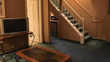 Una sala de estar con televisor, una mesa de centro de vidrio, una escalera y una puerta.