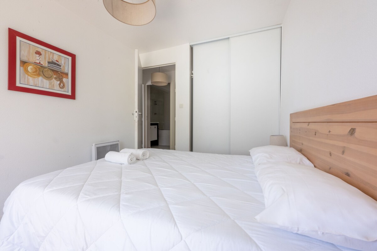 A bedroom with a bed, a wooden headboard, a painting, and a door leading to a bathroom.