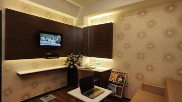 Un cuarto de hotel moderno con una televisión de pantalla plana montada en la pared, una computadora portátil sobre una mesita, un revistero y un florero.