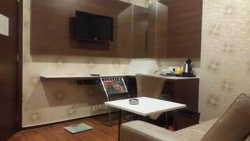 A modern room with a flat-screen TV mounted on the wall, a small table with a lamp, a magazine rack, and a sofa.