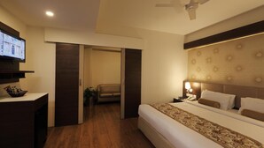 Une chambre d’hôtel moderne avec un grand lit, un téléviseur posé sur un meuble, un bureau avec un panier et un ventilateur de plafond.