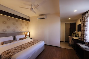 A hotel room with a bed, a ceiling fan, an air conditioning unit, a desk with a chair, and a mirror.