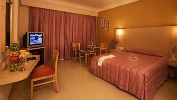 Habitación de hotel con cama, escritorio con televisor, silla, mesita pequeña y mesita de noche.