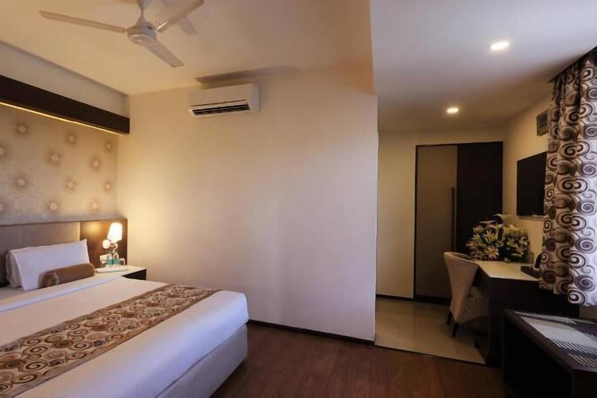 Habitación de hotel con cama, ventilador de techo, equipo de aire acondicionado, escritorio y espejo.
