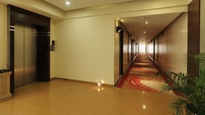 Un couloir d’hôtel avec un tapis rouge, des ascenseurs et une plante.