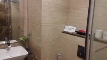 A bathroom with a sink, mirror, shower, and a sign instructing to leave the dustbin after use.