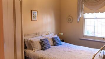 A bedroom with a bed, pillows, a bedside table, a lamp, a window with curtains, and a wall decoration.