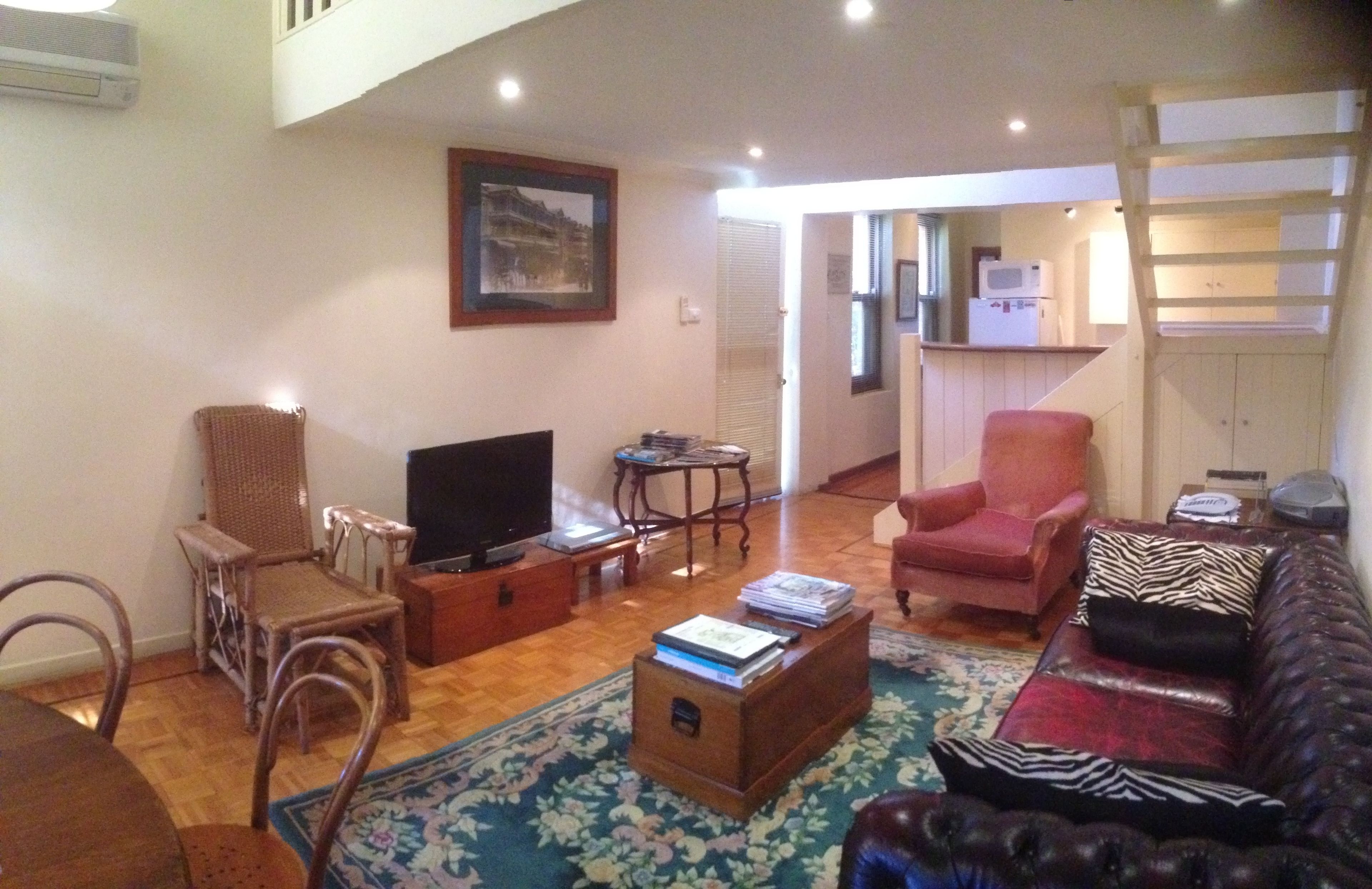 Una sala de estar con televisión, sillas de mimbre, un sillón rojo, un sofá de cuero y una mesa de centro de madera.