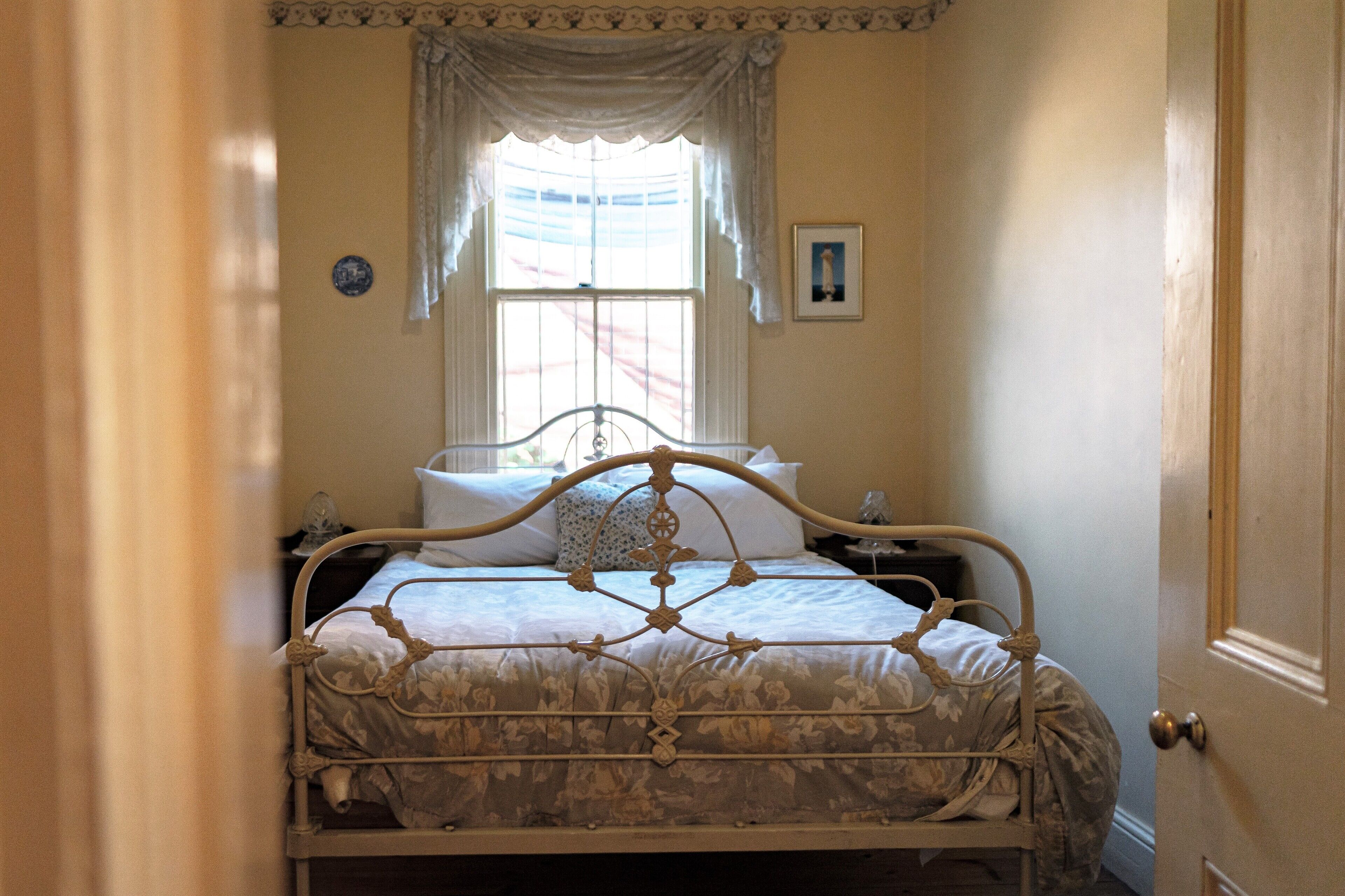 Un dormitorio con una cama, una ventana con cortinas, una mesita de noche y una puerta.