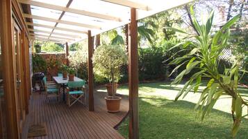 Een overdekt terras met een houten dek, een tafel met stoelen en een potplant.