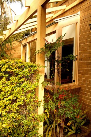 Traditional architecture with a brick facade and wooden pergola, surrounded by lush vegetation.