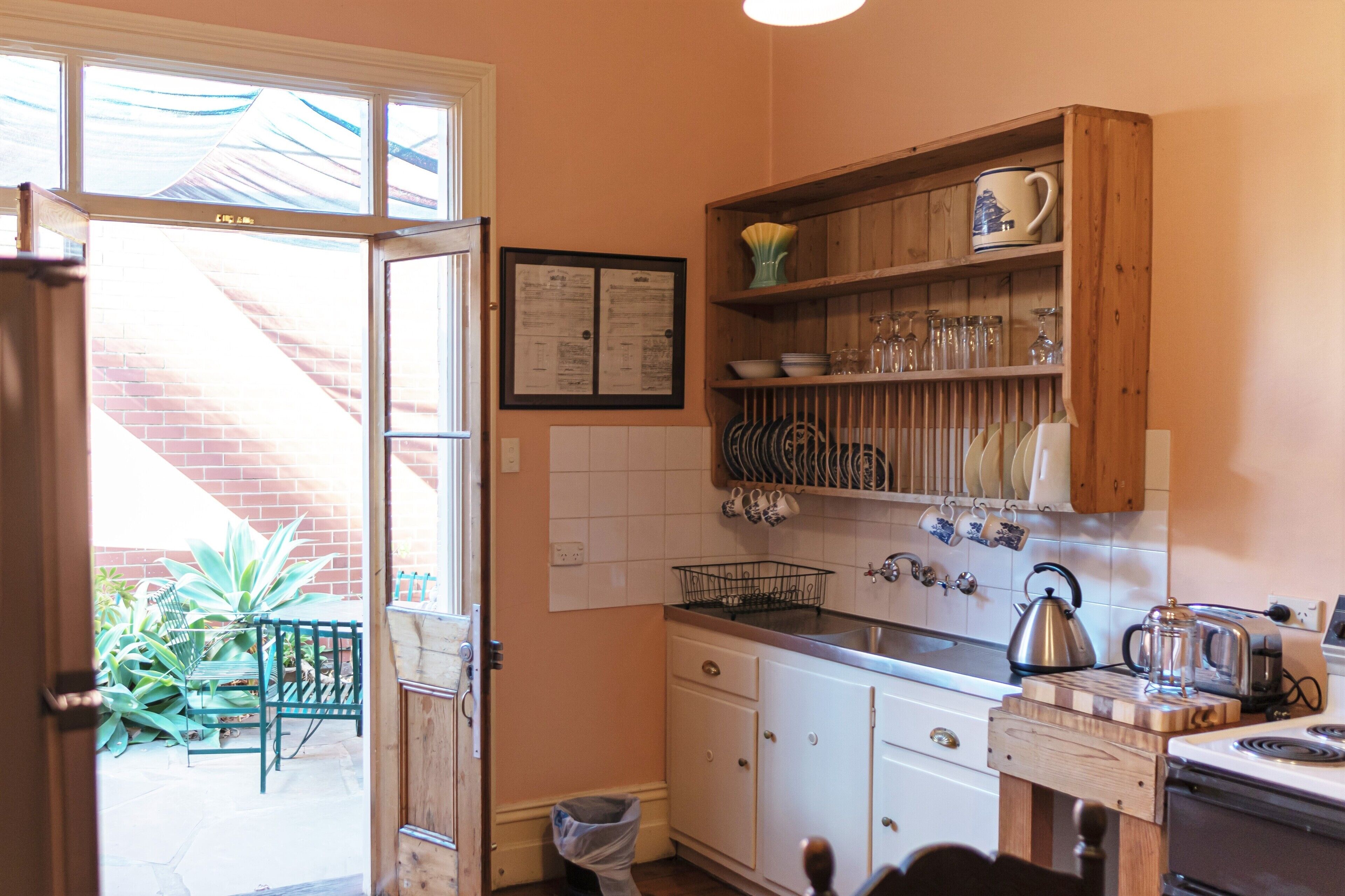 A kitchen with white cabinets, a wooden shelf with dishes, a kettle, and a toaster.