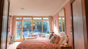 Ein Schlafzimmer mit einem großen Bett, einem Schreibtisch und einem Stuhl. Ein Fenster bietet Blick auf einen Garten.