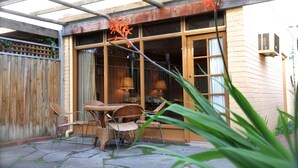 Eine Terrasse mit Korbmöbeln, einem Holzzaun und einem Gebäude mit großen Fenstern und einer Tür.