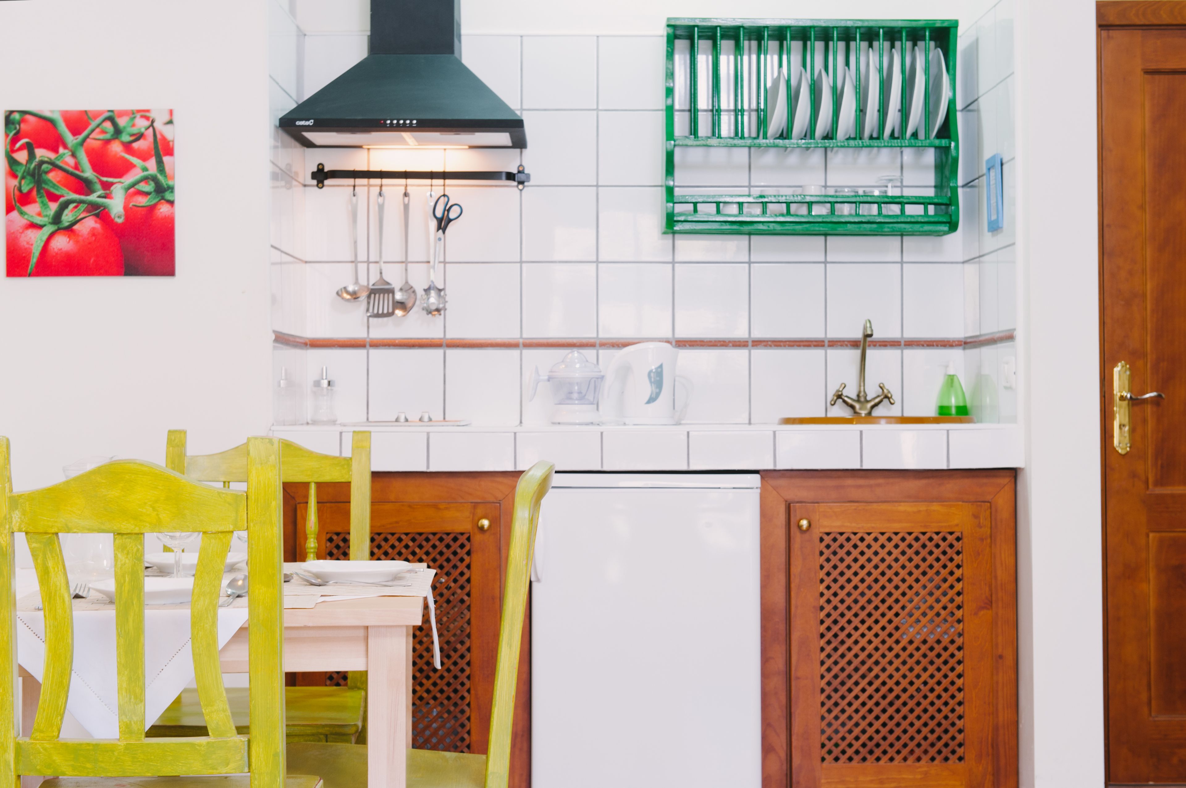 A kitchen with white tiles, a green dish rack, a white refrigerator, and wooden cabinets.