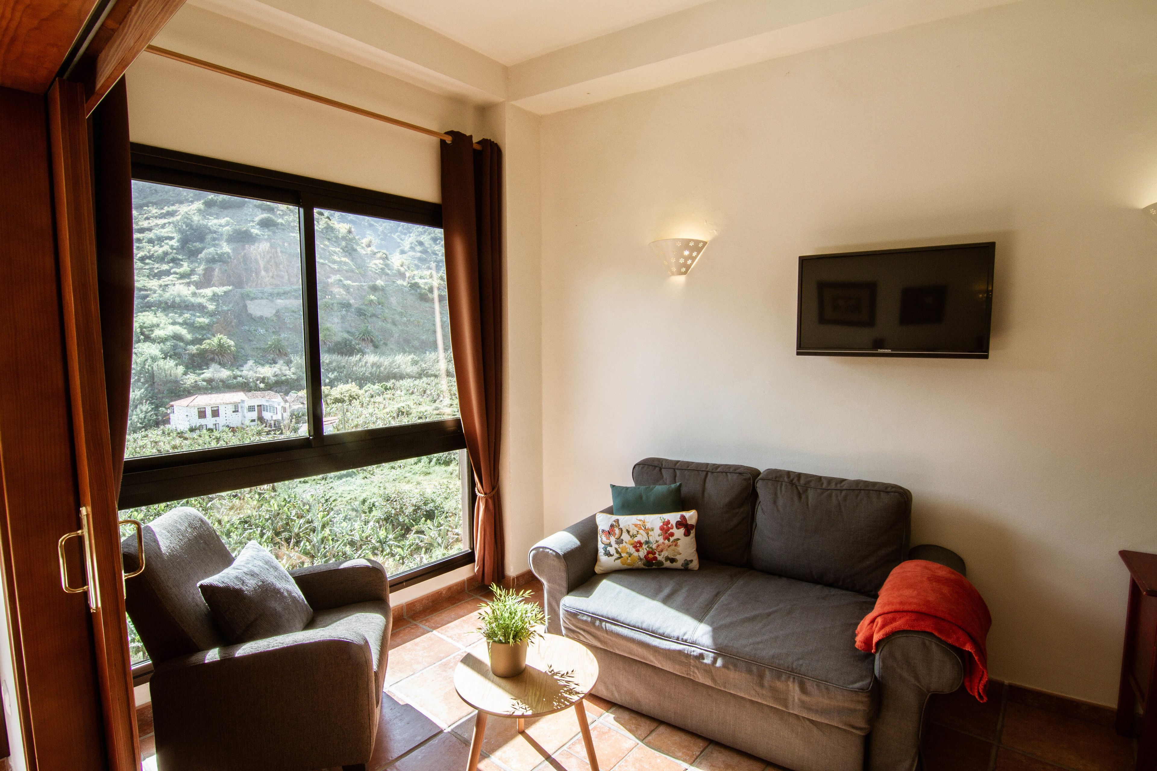A living room with a sofa, two armchairs, a small table with a plant, and a view of greenery outside.