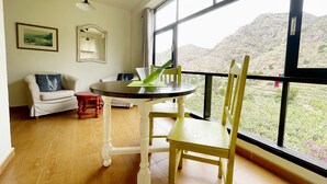 Une pièce comprenant une table à manger, des chaises, un canapé et offrant une vue sur un paysage montagneux grâce à de grandes fenêtres.