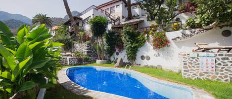 A swimming pool surrounded by a stone wall, with a stone staircase leading up to a building.