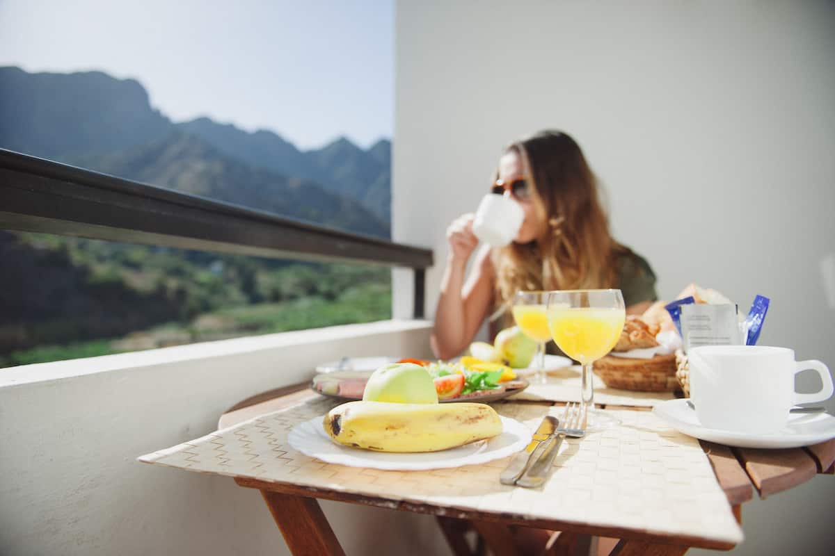 A dining table with a banana, a glass of orange juice, and a cup of coffee, set against a mountain view.