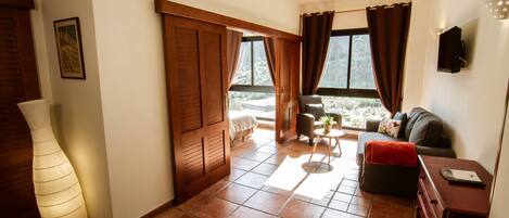 A living room with a sofa, a coffee table, and a TV. There is a door leading to a balcony.