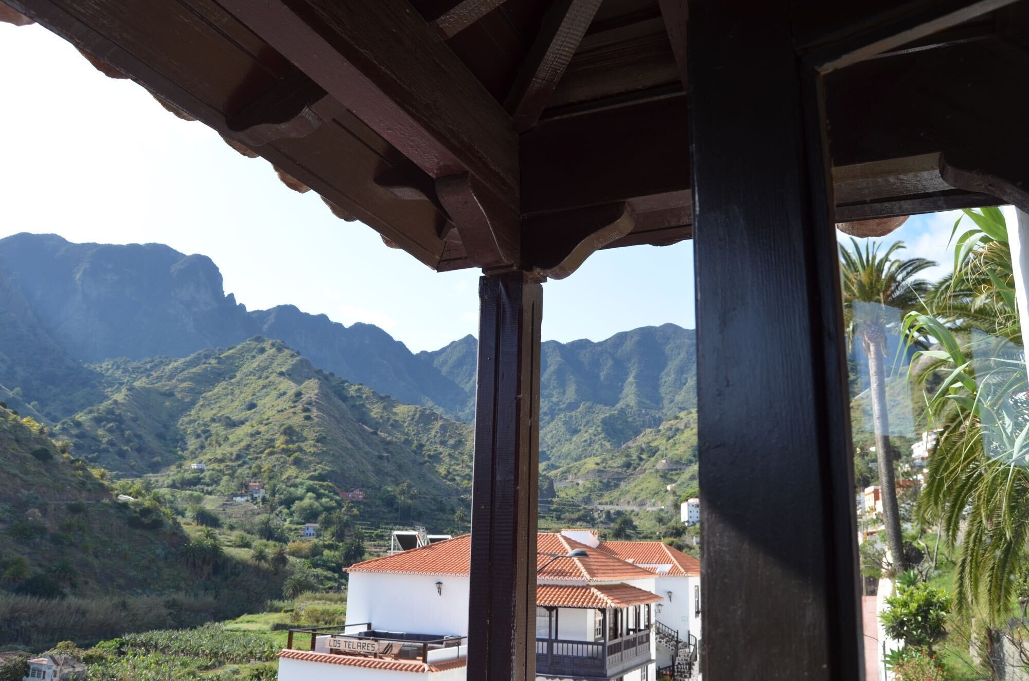A view from a covered balcony overlooking a mountainous landscape with a white building with a red-tiled roof.