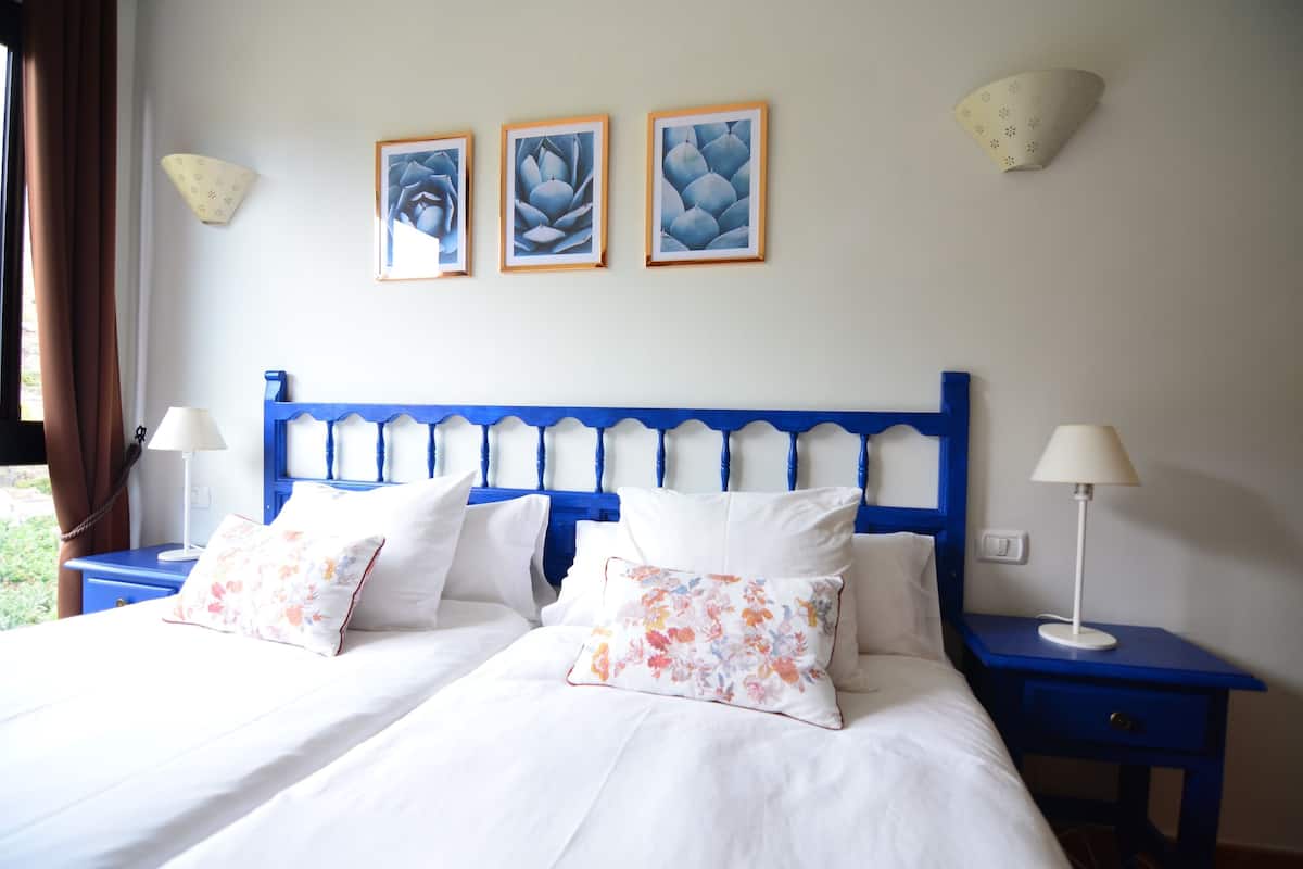 A neatly made bed with white linens and floral pillows, a blue headboard, and two bedside tables with lamps.
