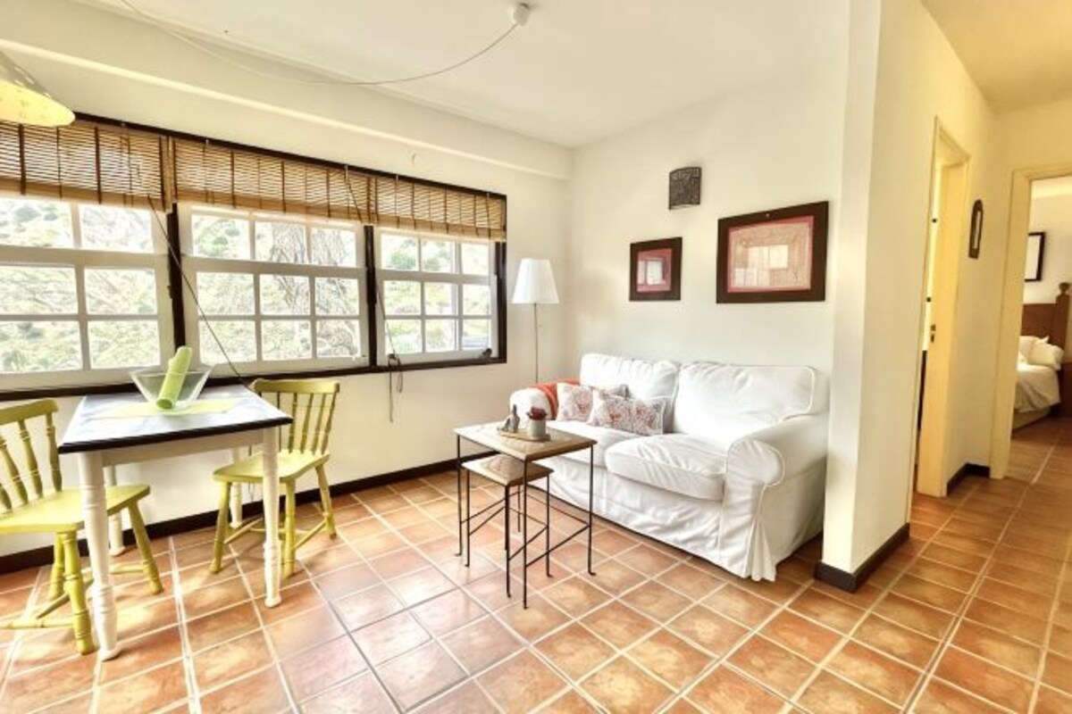 Una habitación con una mesa de comedor, sillas, un sofá blanco y una ventana con persianas.