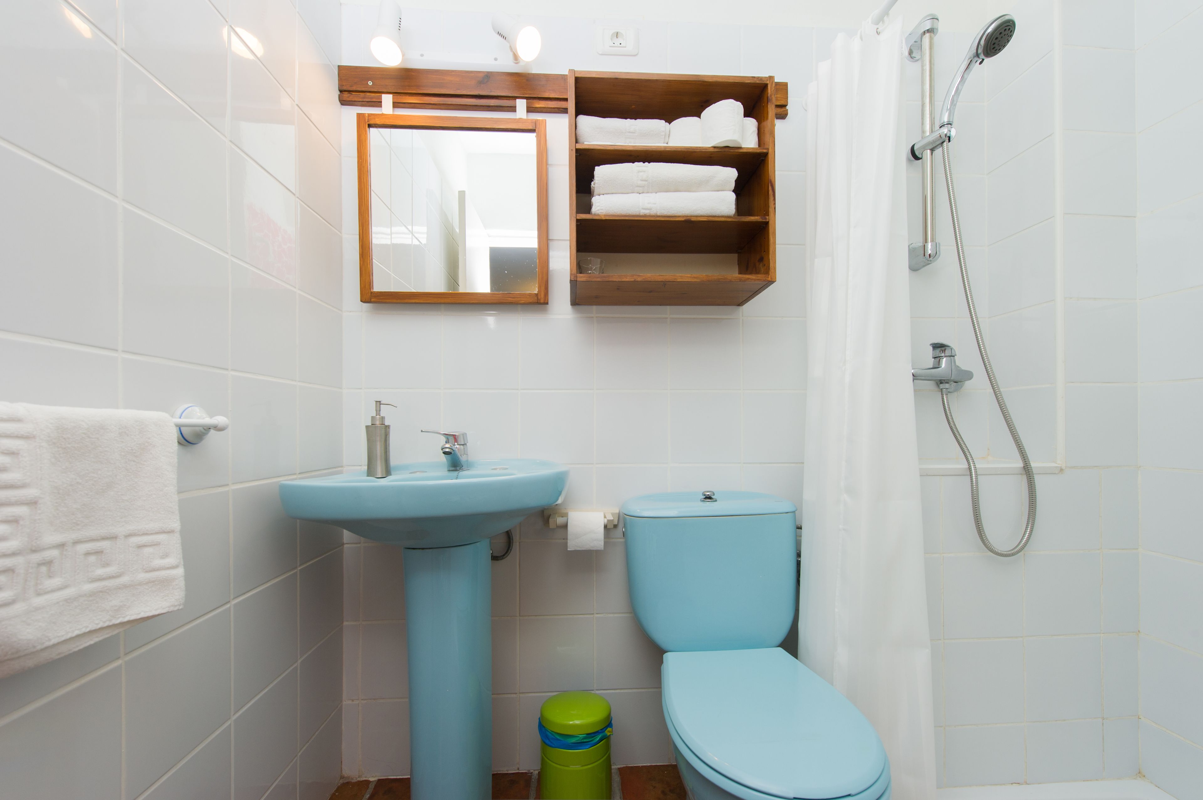 Un baño con lavamanos, inodoro, ducha y un estante con toallas.
