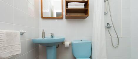 Un baño con lavamanos, inodoro, ducha y un estante con toallas.