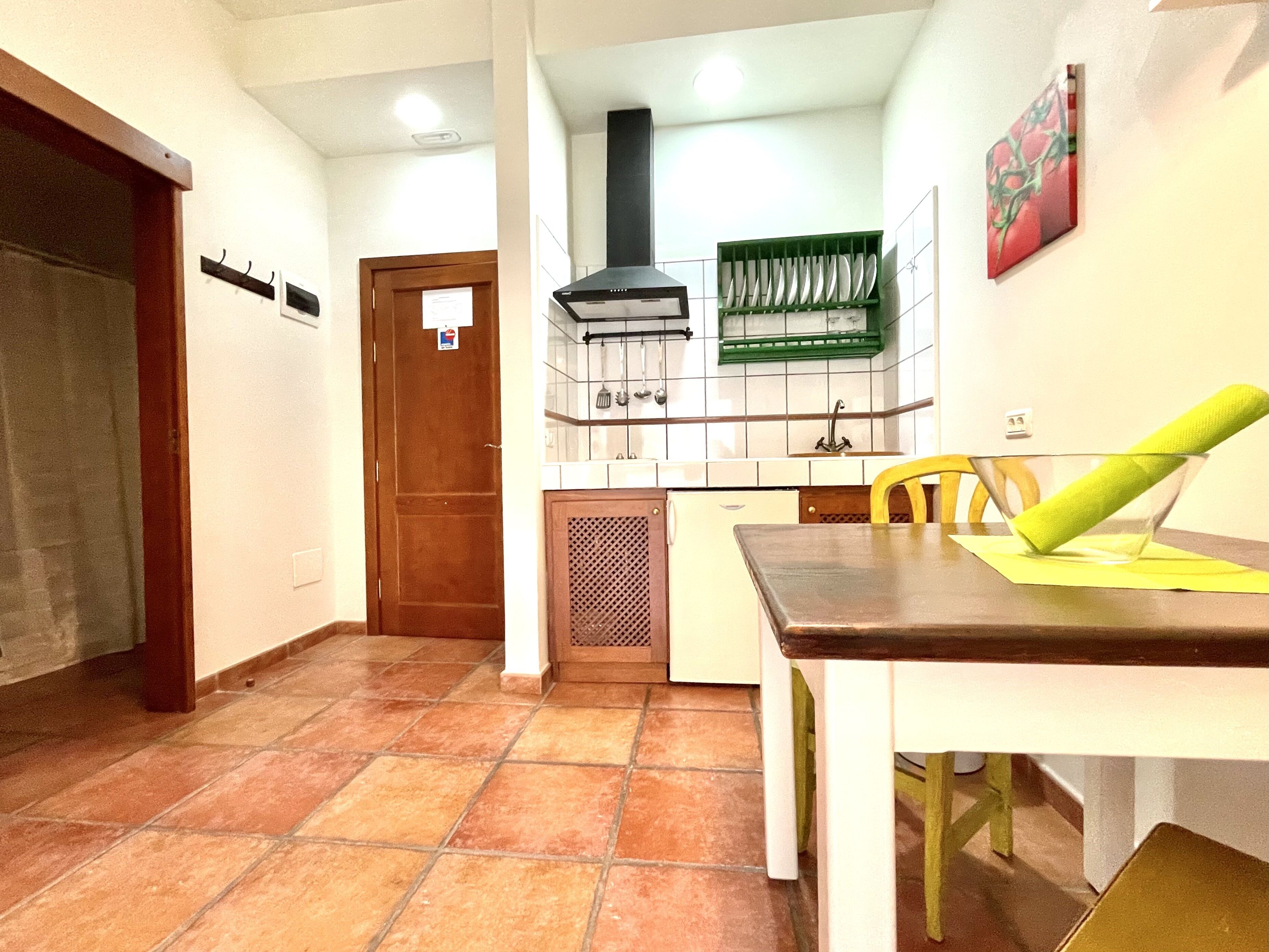 A kitchen with a tiled floor, a dining table with chairs, a green dish rack, and a black range hood.