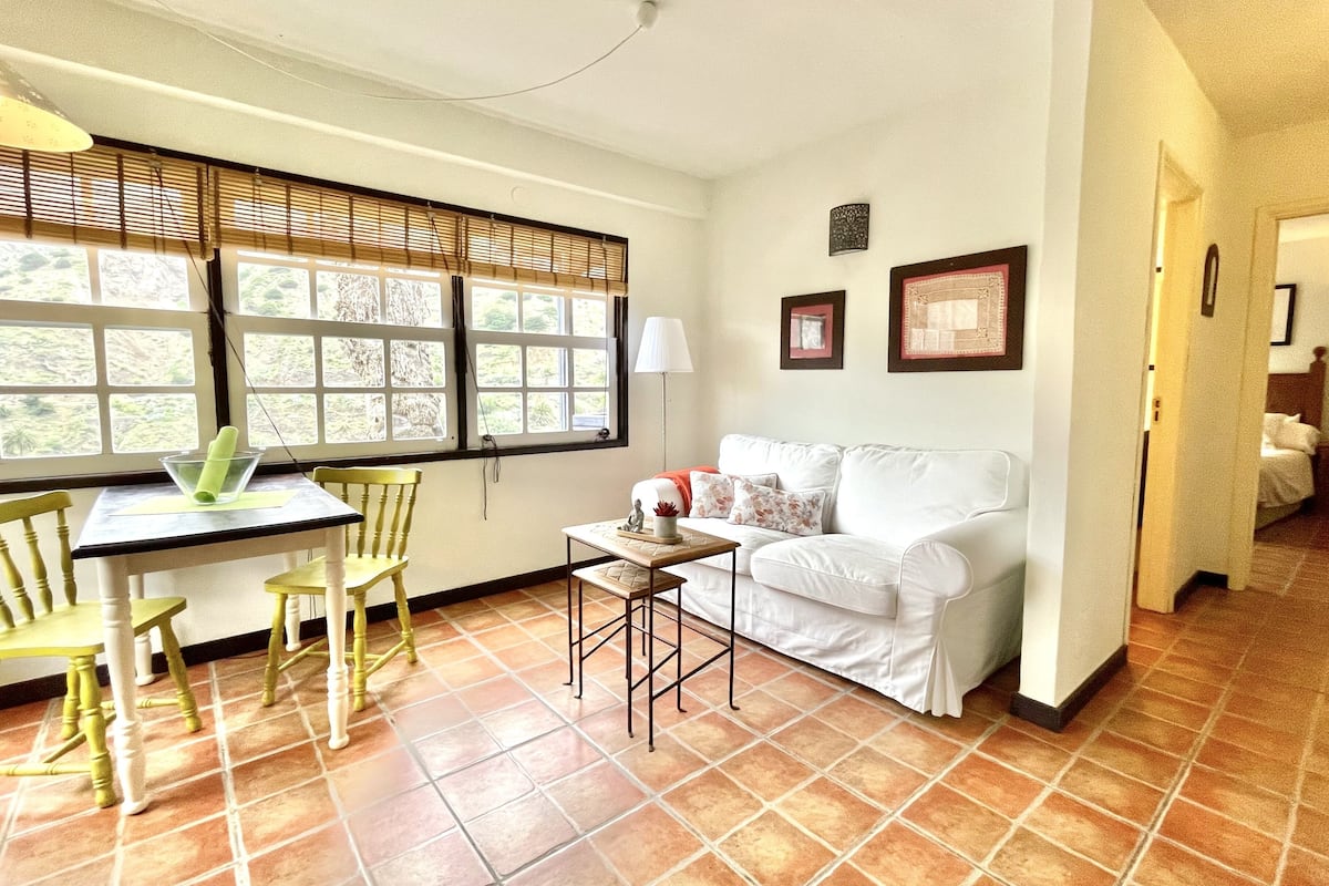 A living room with a white sofa, a dining table with chairs, and a small side table.