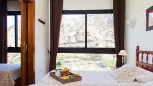 Une chambre à coucher avec un lit, une table de chevet, une fenêtre avec des rideaux et une vue sur un paysage montagneux.