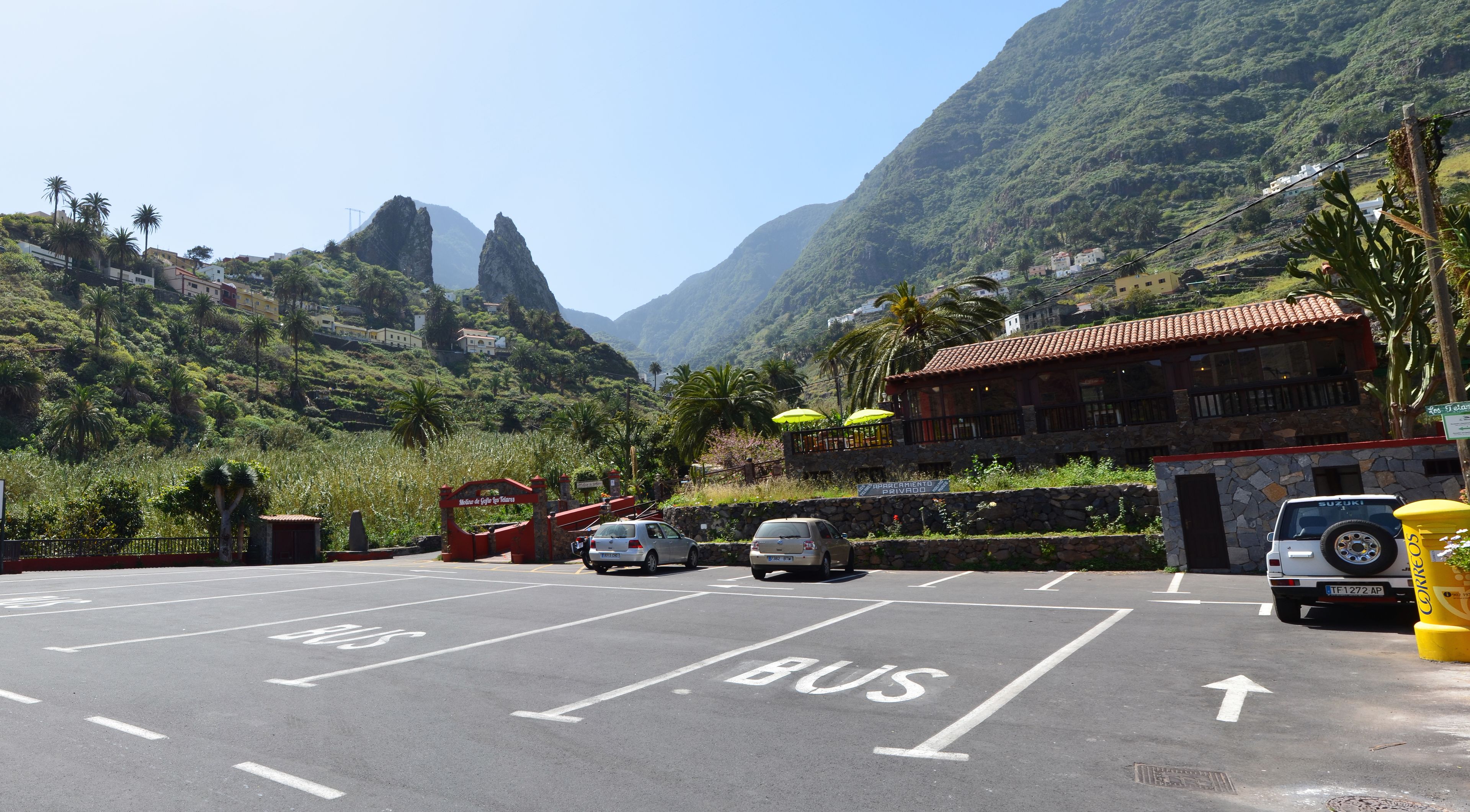 Un'area di parcheggio con corsie riservate agli autobus, un edificio con tetto rosso e montagne sullo sfondo.