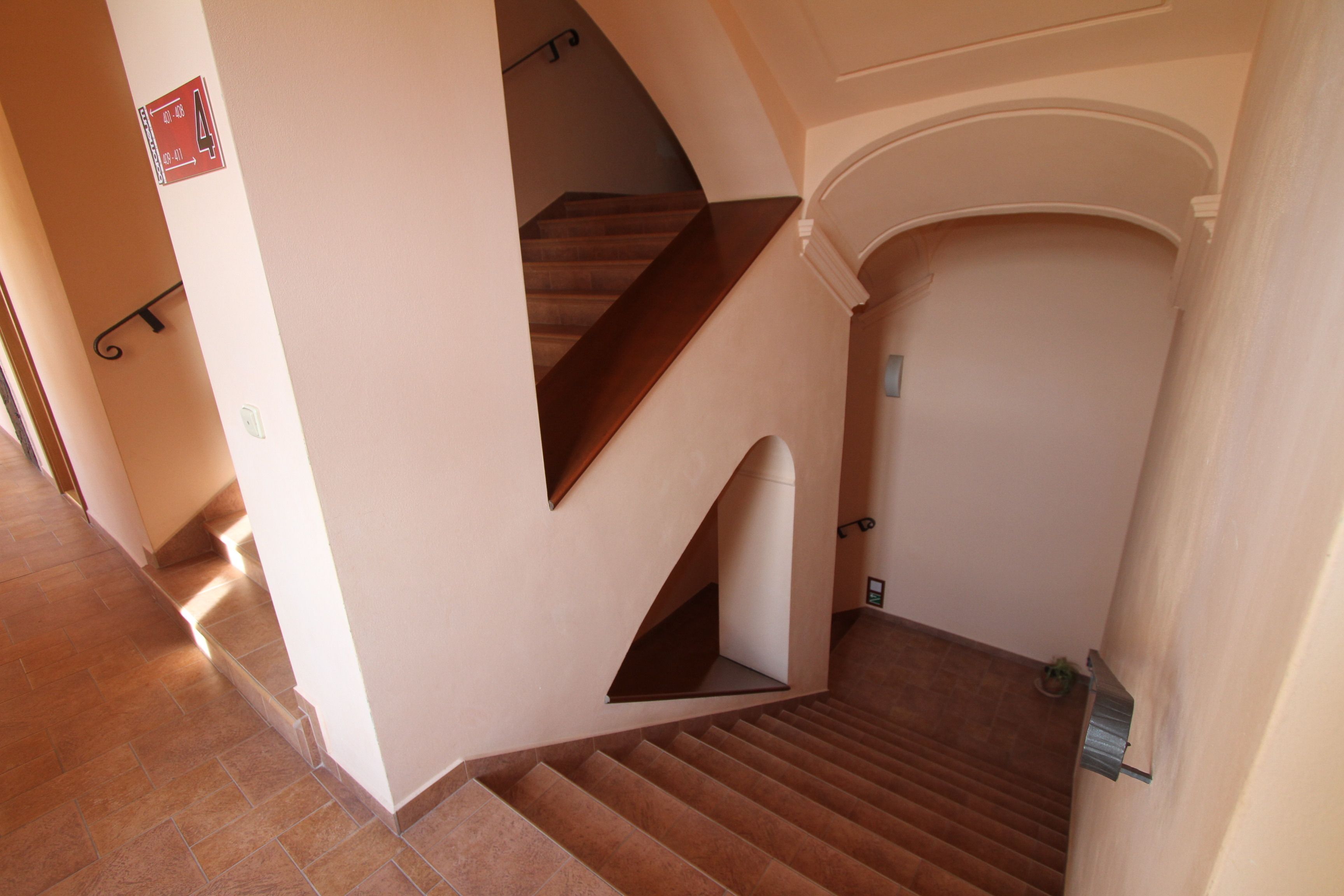 A staircase with a wooden finish, a landing with a small plant, and a red sign with numbers on the wall.