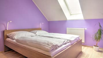 A bedroom with a sloped ceiling, a bed with white linens, a radiator, and a potted plant.
