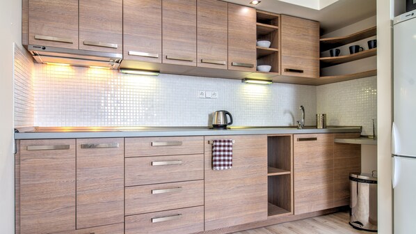 A modern kitchen with wooden cabinets, a tiled backsplash, and stainless steel appliances. - Boromeum Residence (Hradec Kralove)