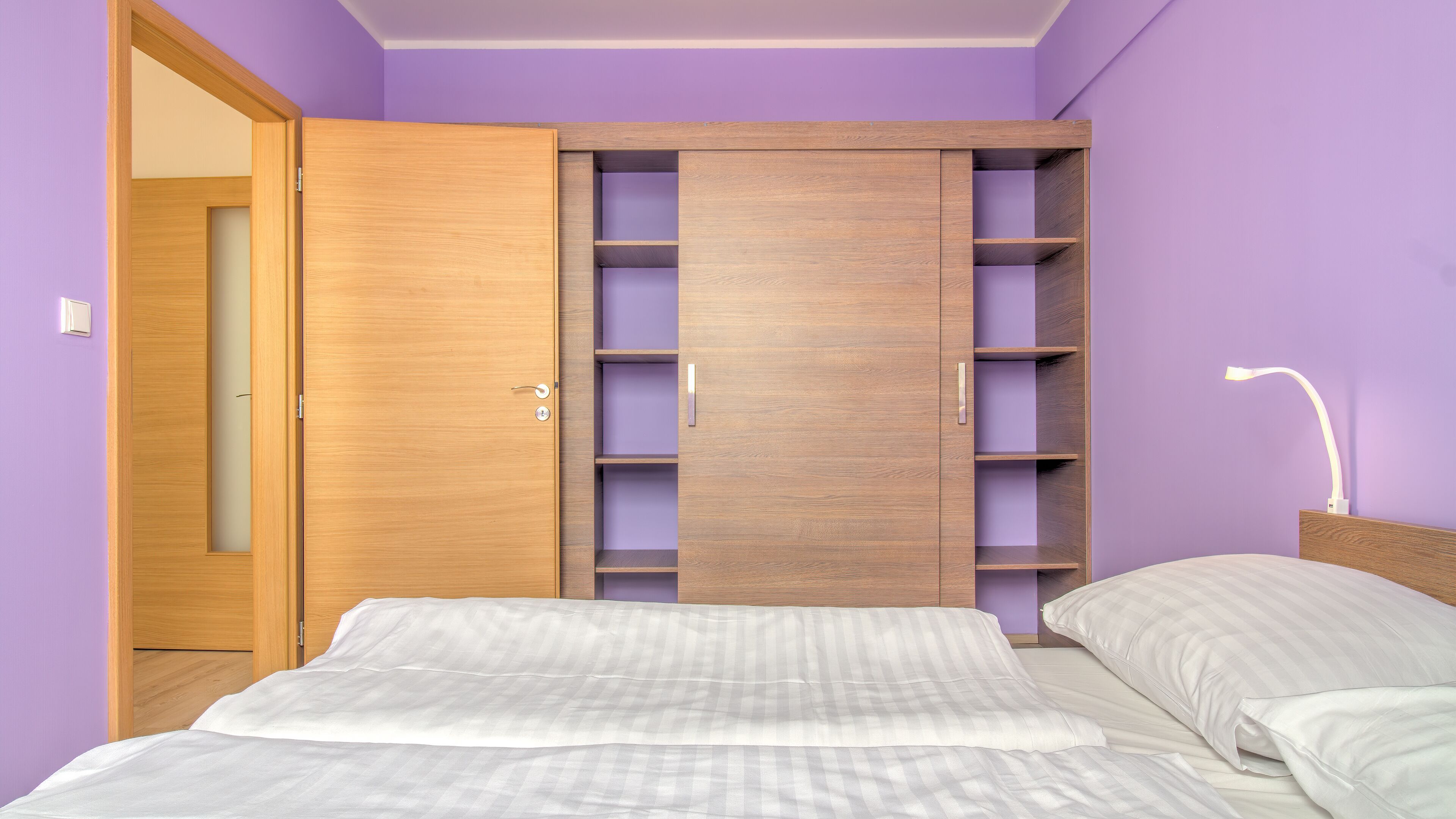 Un dormitorio con una cama, un armario con estantes múltiples y una lámpara de noche.