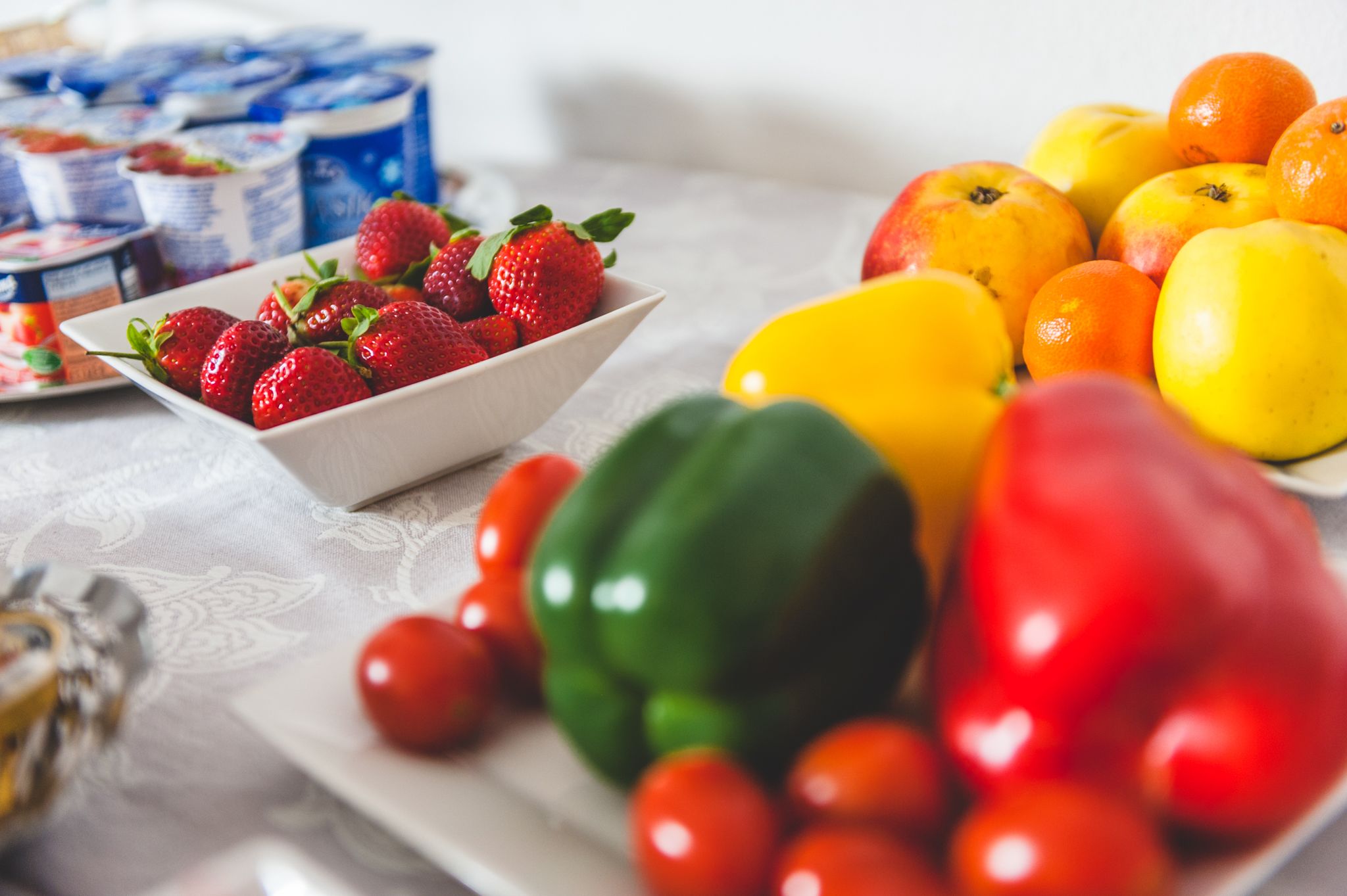 A table with a variety of fruits and vegetables, including strawberries, apples, oranges, and tomatoes.