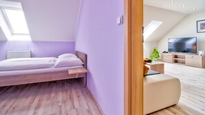 A modern bedroom with a sloped ceiling, a bed, a wooden nightstand, a TV, and a plant.