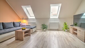 A modern loft apartment with a grey sofa, a wooden coffee table, a potted plant, and a TV on a wooden stand.