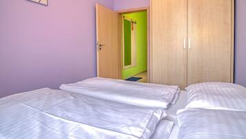A bedroom with two beds, a wooden wardrobe, and a green door.