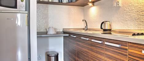 A modern kitchen with a microwave, kettle, and stainless steel sink.