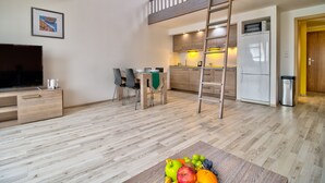 A modern living room with a TV, wooden furniture, a dining area, and a kitchen with a ladder.
