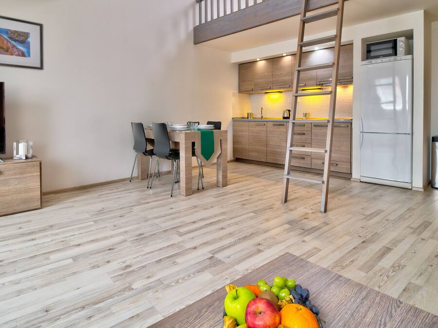 A modern living room with a TV, wooden furniture, a dining area, and a kitchen with a ladder.