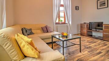 Una sala de estar con un sofá, una mesa de centro de vidrio, un televisor y un mueble de madera.