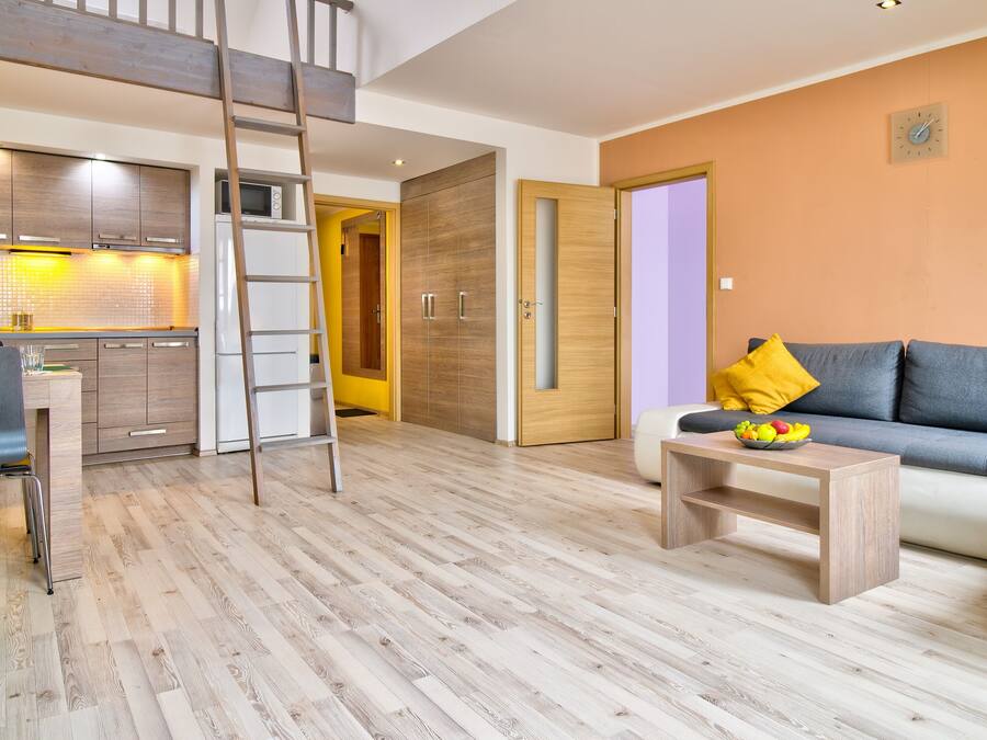 A modern living room with a sofa, a coffee table with fruit, a kitchen area with a microwave, and a wooden floor.